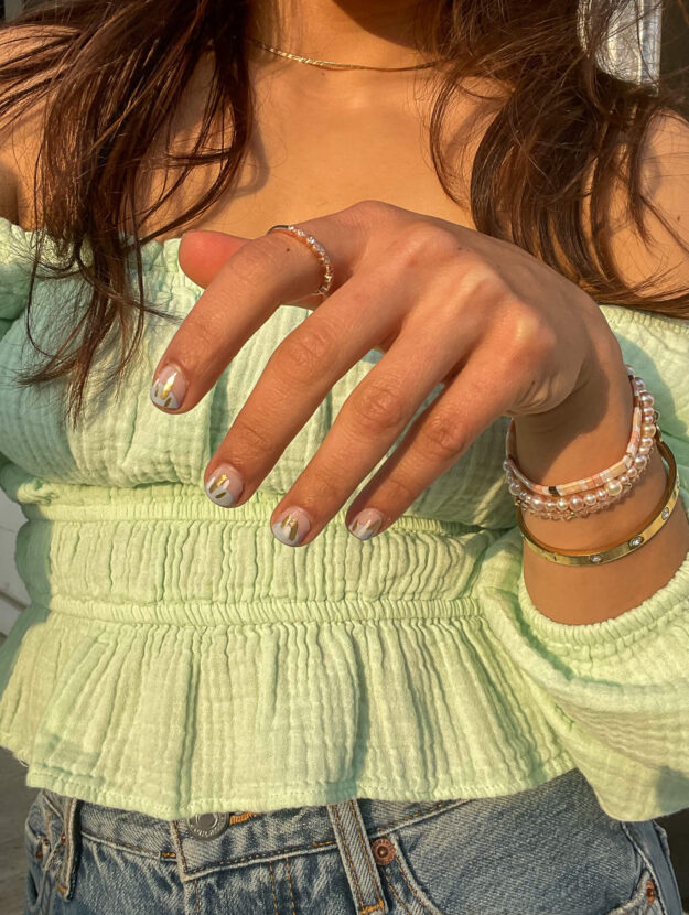 close up of a woman wearing a green off the shoulder top showing her printed nails and beaded bracelets